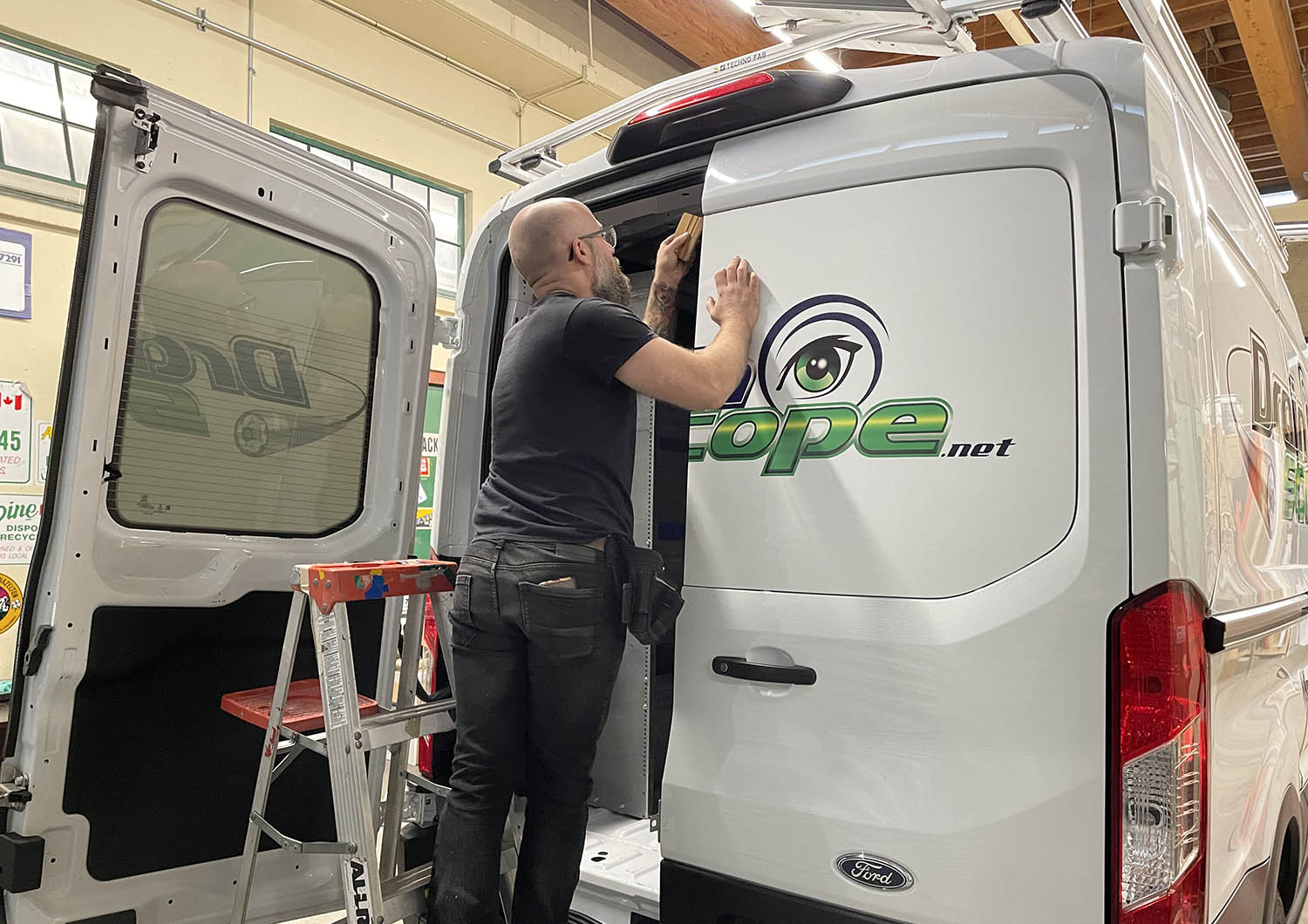 Worker applying a vinyl decal to the back of a white vehicle
